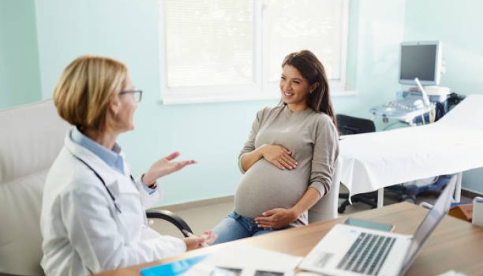 Happy expecting woman communicating with her female gynecologist during a visit in the office.